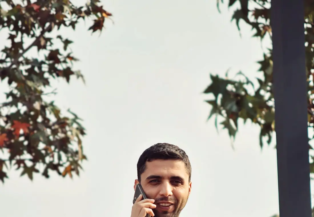 A man taking a phone call outdoors under a tree in a park